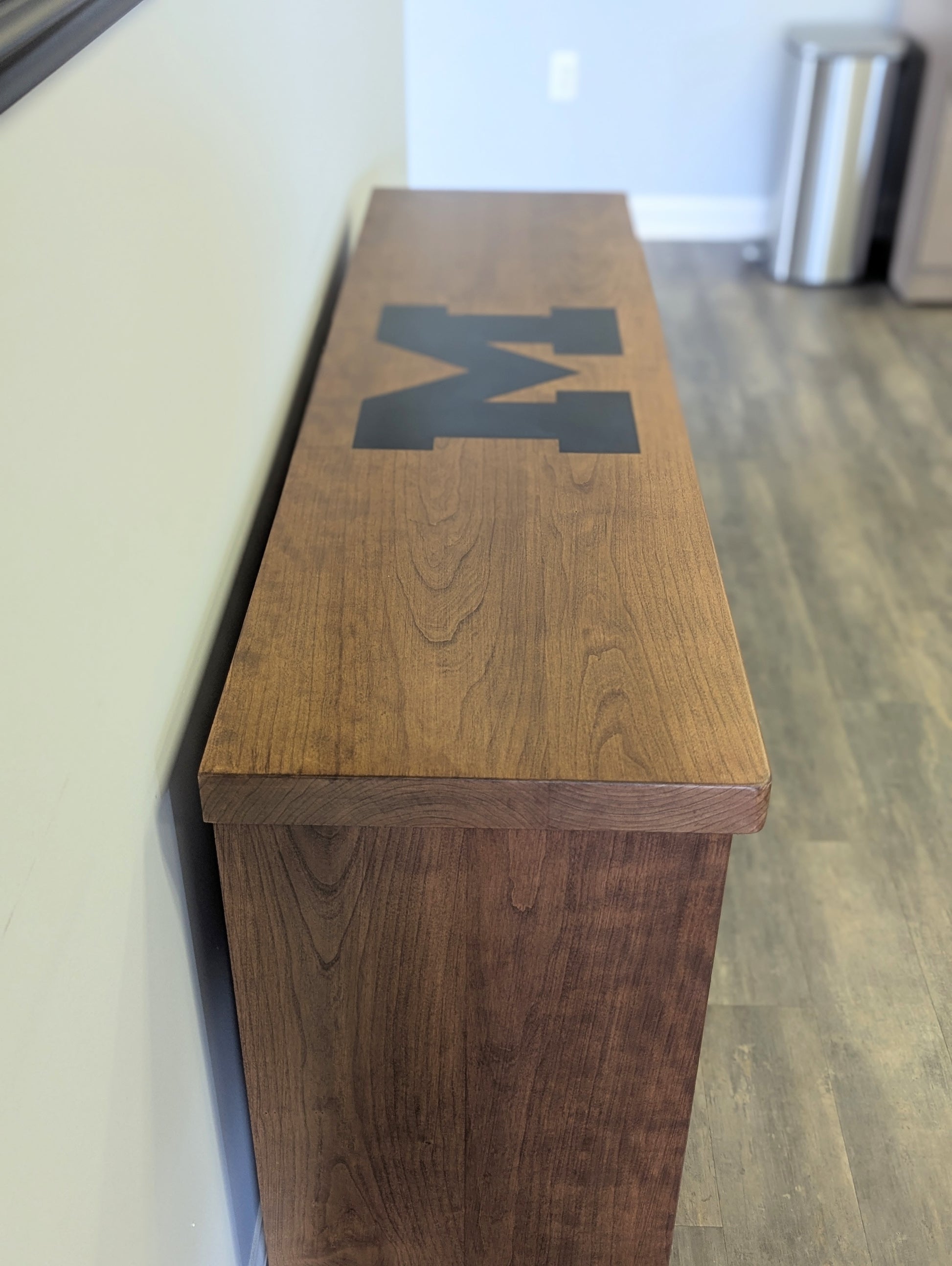 A modern stained cherry hardwood credenza with University of Michigan epoxy inlay on tabletop, three cabinets with gold handle finishes and interior storage for organizing office supplies.