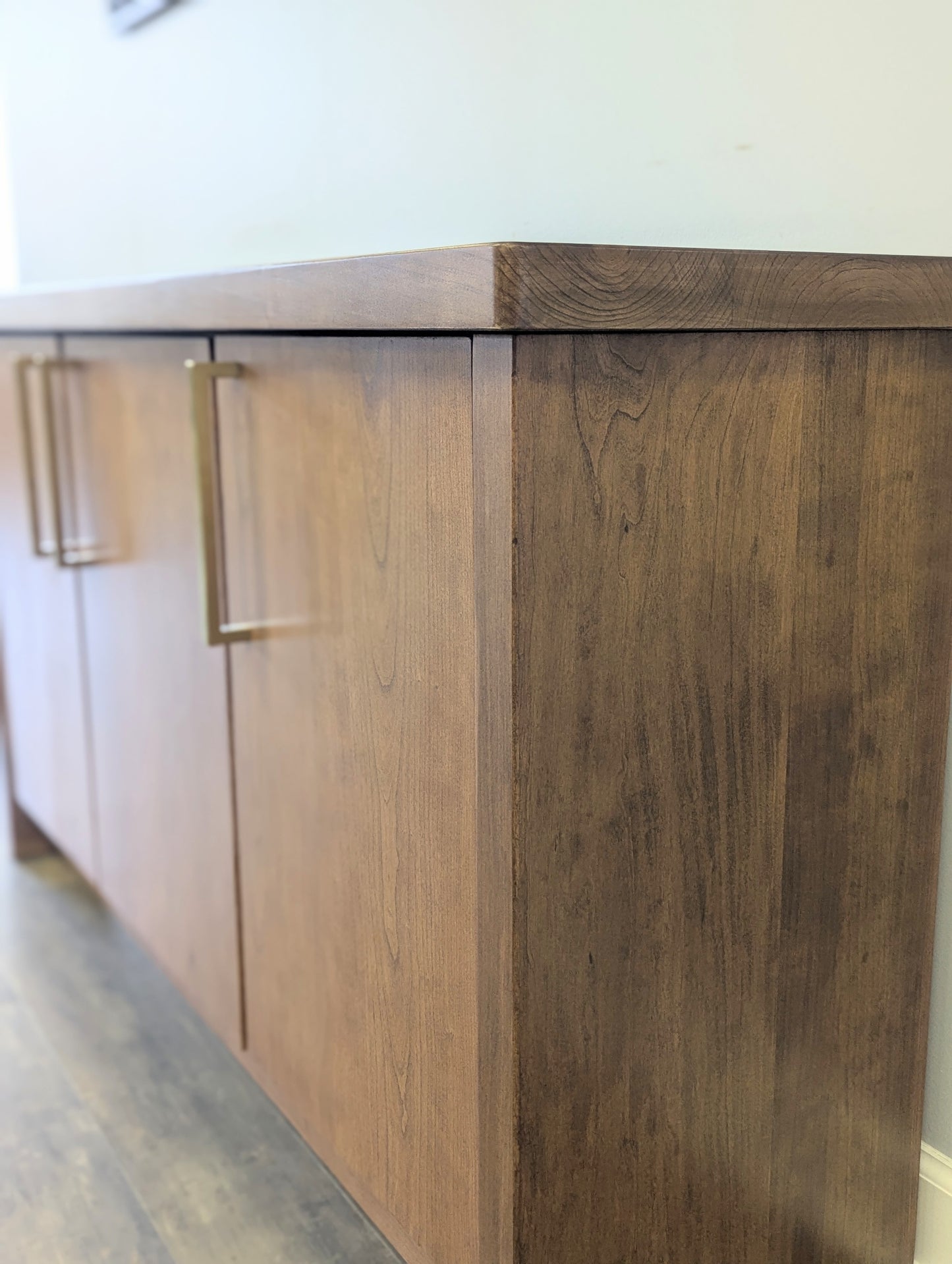 A modern stained cherry hardwood credenza with University of Michigan epoxy inlay on tabletop, three cabinets with gold handle finishes and interior storage for organizing office supplies.