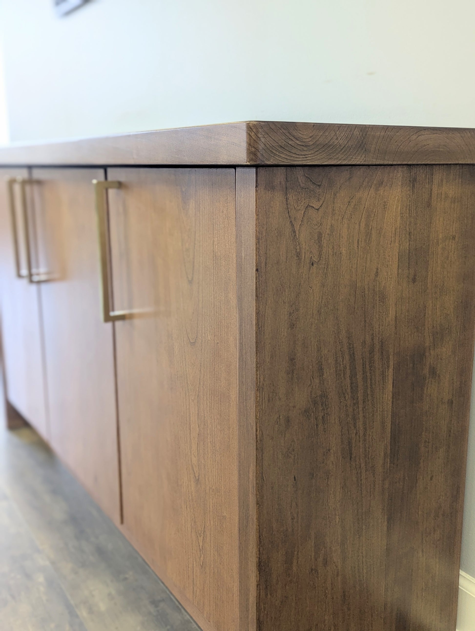 A modern stained cherry hardwood credenza with University of Michigan epoxy inlay on tabletop, three cabinets with gold handle finishes and interior storage for organizing office supplies.