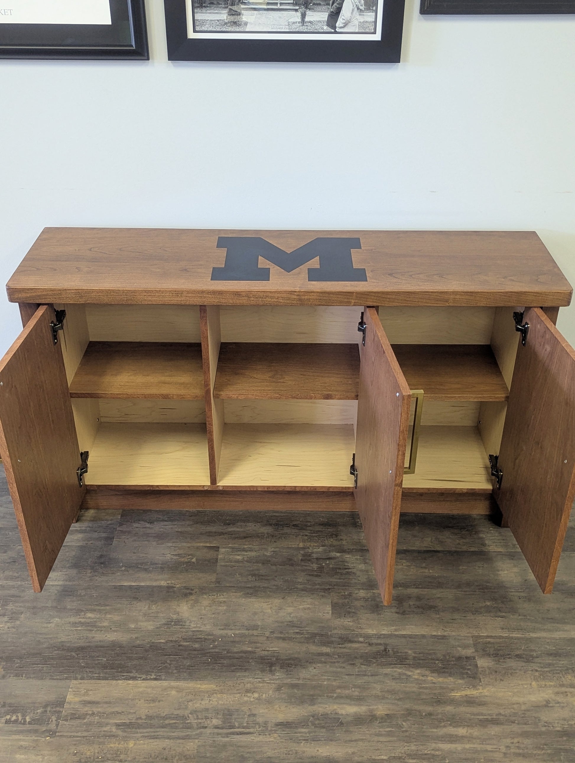 A modern stained cherry hardwood credenza with University of Michigan epoxy inlay on tabletop, three cabinets with gold handle finishes and interior storage for organizing office supplies.