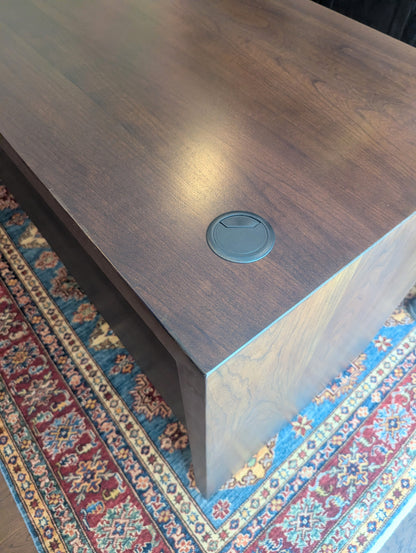 A modern stained cherry hardwood executive desk with waterfall style sides, grommets in the desk top and a hidden cord management shelf for clean storage.