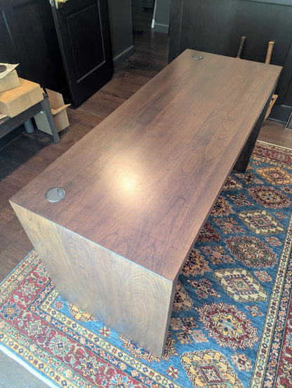 A modern stained cherry hardwood executive desk with waterfall style sides, grommets in the desk top and a hidden cord management shelf for clean storage.