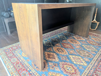 A modern stained cherry hardwood executive desk with waterfall style sides, grommets in the desk top and a hidden cord management shelf for clean storage.