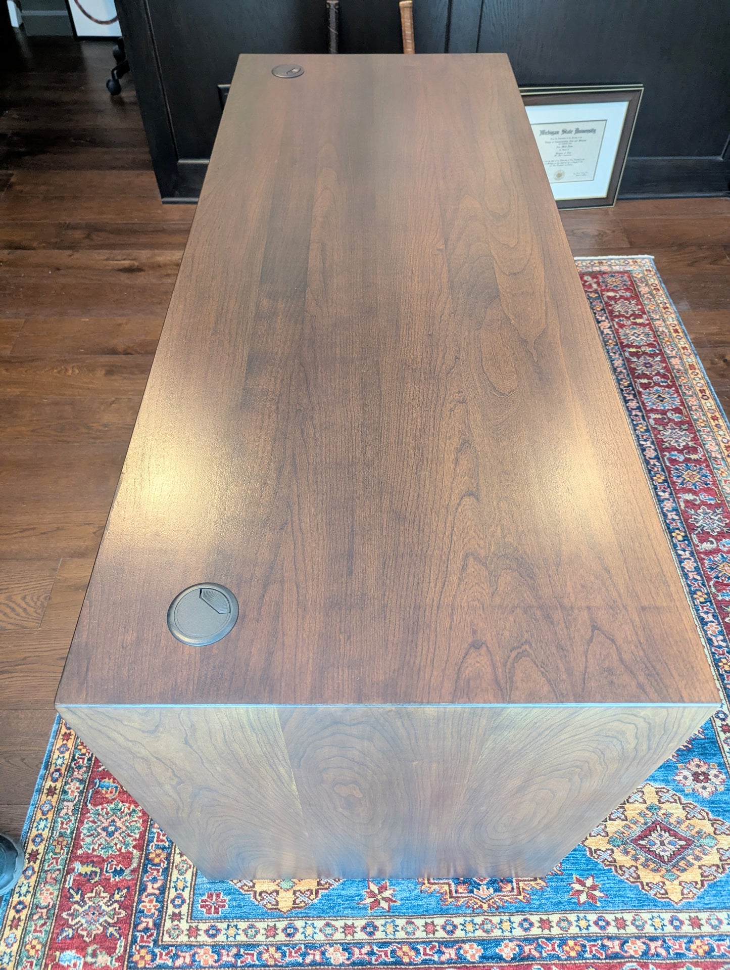 A modern stained cherry hardwood executive desk with waterfall style sides, grommets in the desk top and a hidden cord management shelf for clean storage.