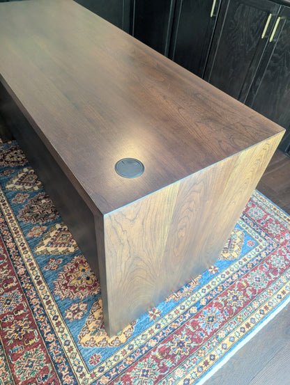 A modern stained cherry hardwood executive desk with waterfall style sides, grommets in the desk top and a hidden cord management shelf for clean storage.