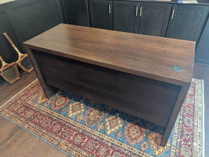 A modern stained cherry hardwood executive desk with waterfall style sides, grommets in the desk top and a hidden cord management shelf for clean storage.
