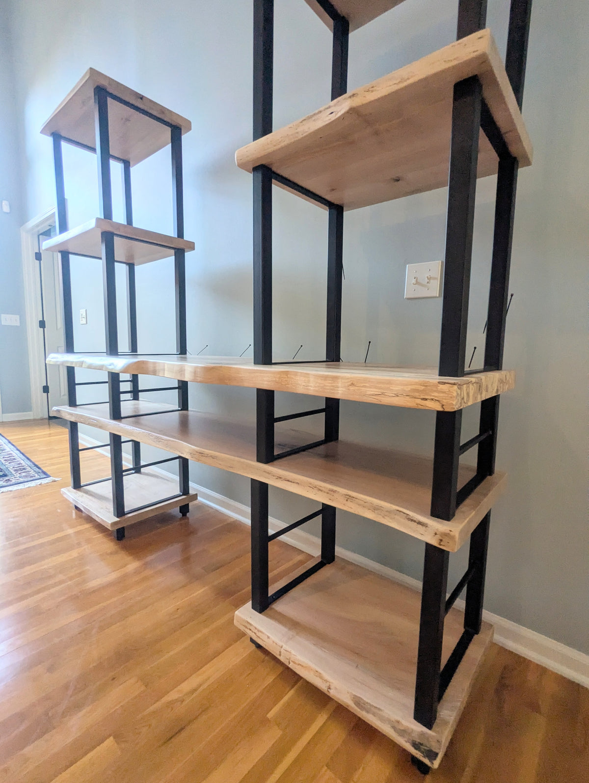 Live edge rustic ambrosia maple hardwood shelving unit with five shelves and custom fabricated black metal bars for storage of vinyl records, CDs, and corresponding players and speakers in a modern home living room.