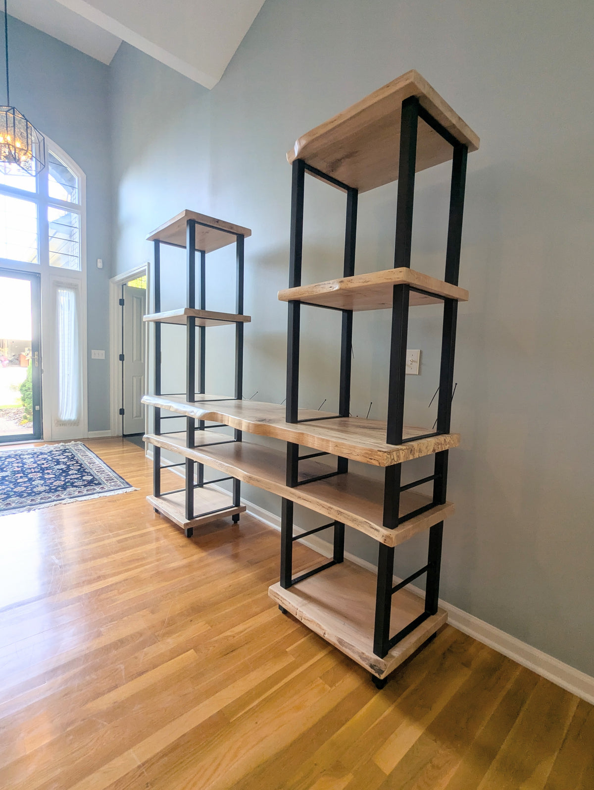 Live edge rustic ambrosia maple hardwood shelving unit with five shelves and custom fabricated black metal bars for storage of vinyl records, CDs, and corresponding players and speakers in a modern home living room.