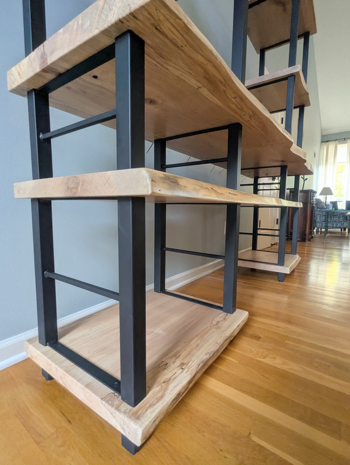 Live edge rustic ambrosia maple hardwood shelving unit with five shelves and custom fabricated black metal bars for storage of vinyl records, CDs, and corresponding players and speakers in a modern home living room.