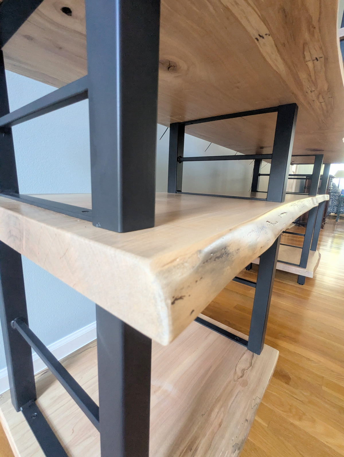 Live edge rustic ambrosia maple hardwood shelving unit with five shelves and custom fabricated black metal bars for storage of vinyl records, CDs, and corresponding players and speakers in a modern home living room.