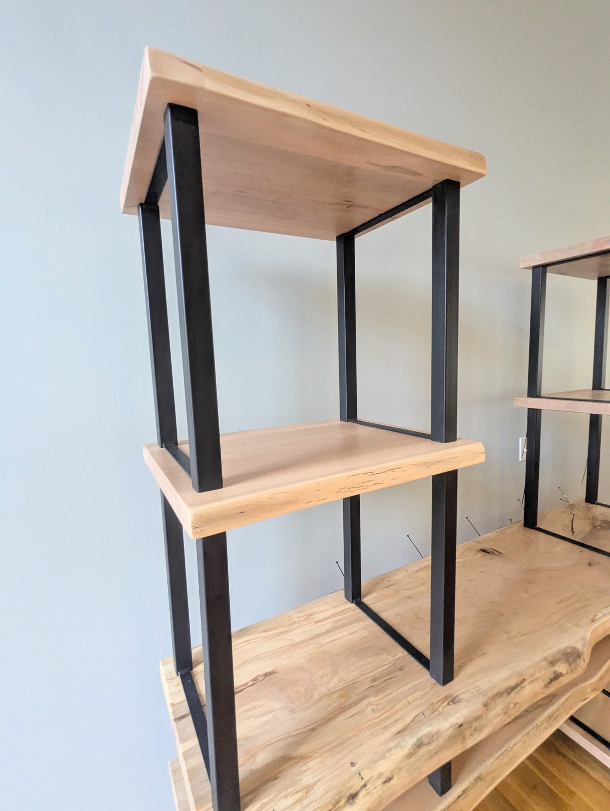 Live edge rustic ambrosia maple hardwood shelving unit with five shelves and custom fabricated black metal bars for storage of vinyl records, CDs, and corresponding players and speakers in a modern home living room.