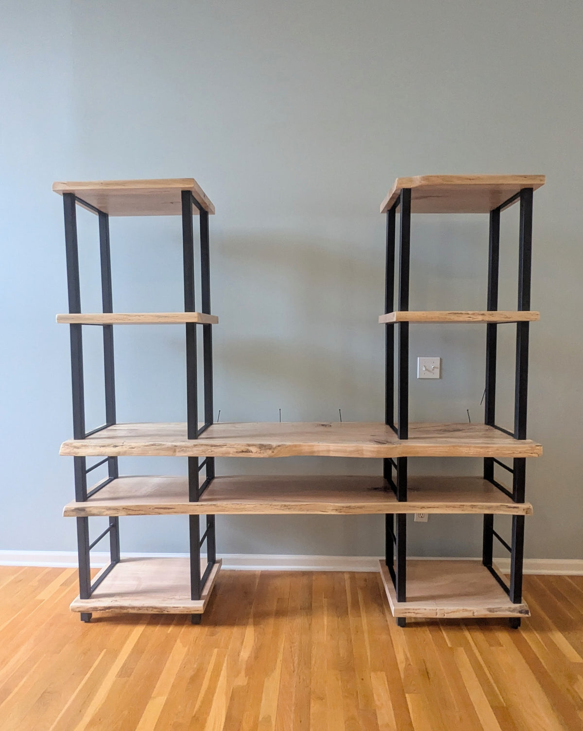 Live edge rustic ambrosia maple hardwood shelving unit with five shelves and custom fabricated black metal bars for storage of vinyl records, CDs, and corresponding players and speakers in a modern home living room.