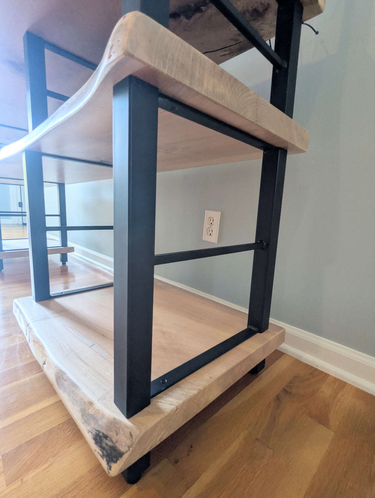 Live edge rustic ambrosia maple hardwood shelving unit with five shelves and custom fabricated black metal bars for storage of vinyl records, CDs, and corresponding players and speakers in a modern home living room.