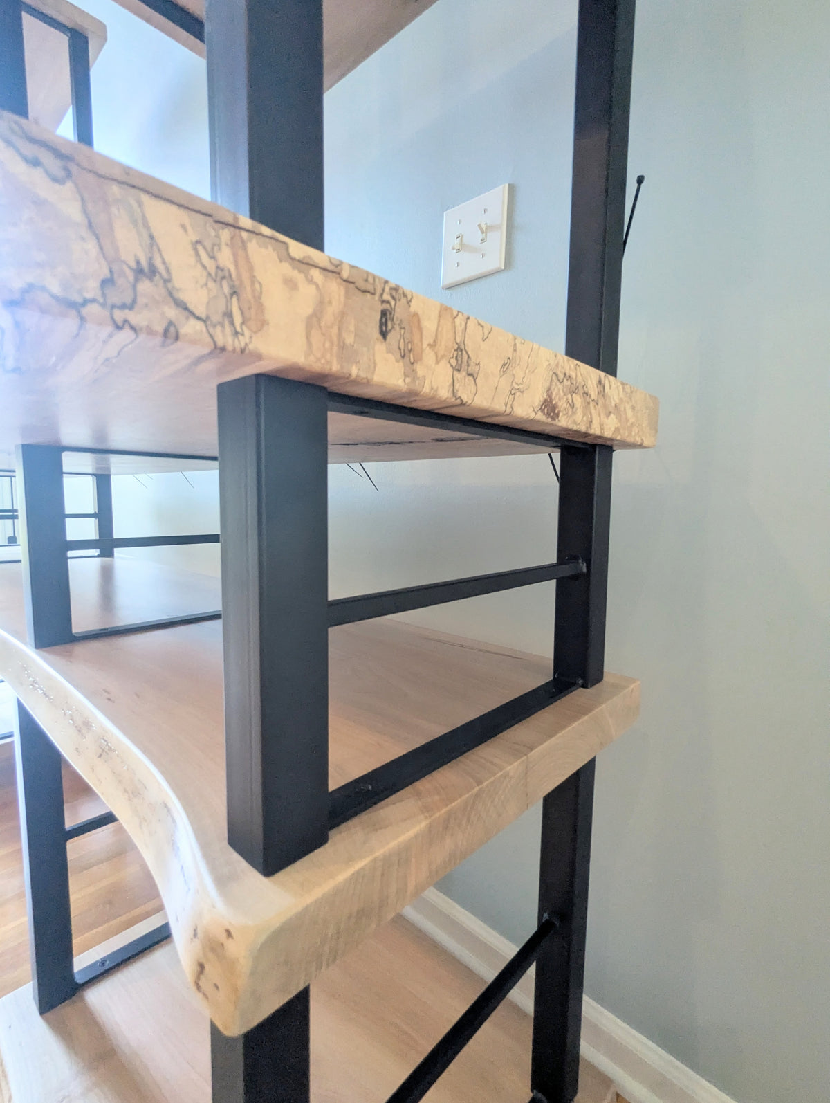 Live edge rustic ambrosia maple hardwood shelving unit with five shelves and custom fabricated black metal bars for storage of vinyl records, CDs, and corresponding players and speakers in a modern home living room.