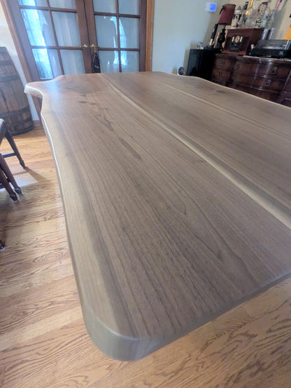 Rustic live edge walnut hardwood dining table with wood legs and a natural finish.