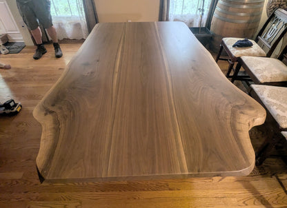 Rustic live edge walnut hardwood dining table with wood legs and a natural finish.