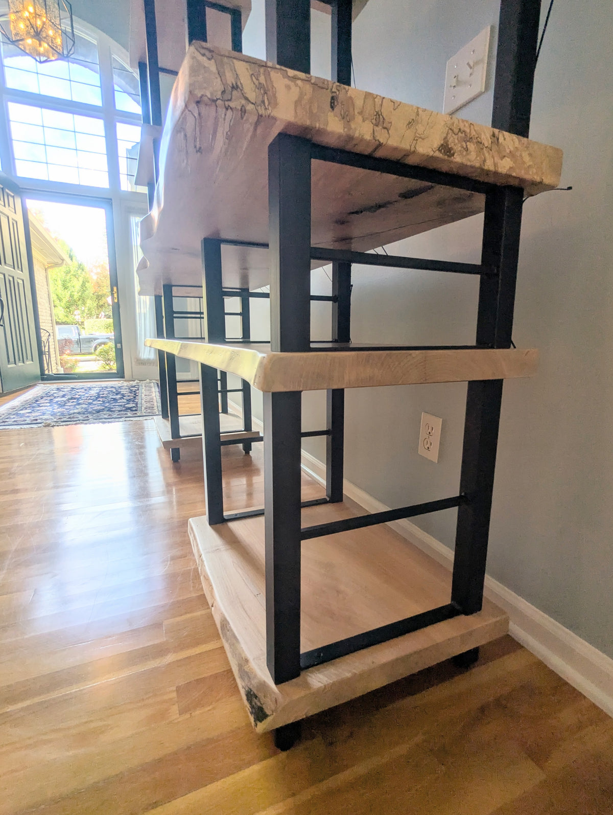Live edge rustic ambrosia maple hardwood shelving unit with five shelves and custom fabricated black metal bars for storage of vinyl records, CDs, and corresponding players and speakers in a modern home living room.